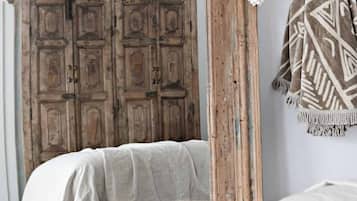 A bedroom with a rustic wooden wardrobe, a bed with a white and gray blanket, and a patterned throw blanket on a chair.