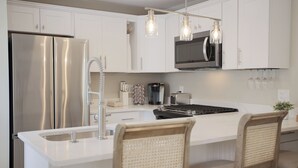 A modern kitchen with white cabinetry, stainless steel appliances, a central island with bar stools, and pendant lighting. - Beautiful Cottage with Water Views - 2 Bedrooms (Delanco)