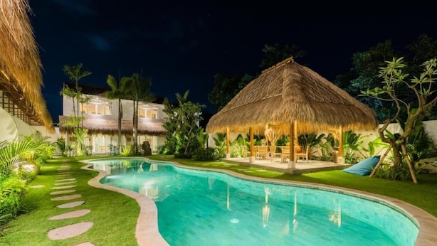 A swimming pool with a thatched-roof structure and a lounge area with outdoor seating. - Baan Seanok lofts (Pecatu)