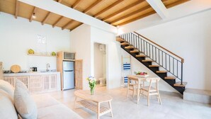 A spacious living area with a wooden staircase, a kitchen with modern appliances, and a dining area with a table and chairs. - Baan Seanok lofts (Pecatu)