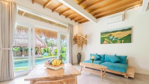 A room with a wooden ceiling, a sofa with blue cushions, a wooden table with fruit, and a painting of a landscape. - Baan Seanok lofts (Pecatu)