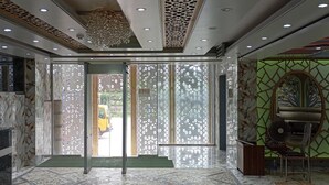 Un hall d’hôtel avec un comptoir d’accueil, une moquette verte et un mur décoratif orné de motifs géométriques.