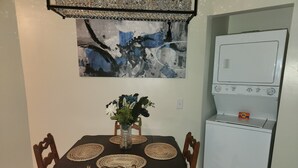 A dining area with a table set for four, a vase with flowers, a painting on the wall, and a white refrigerator. - Quiet and sophisticated apartment with AC in Clinton (Clinton)