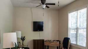 A living room with a ceiling fan, a flat-screen TV, a foosball table, a sofa, a coffee table, and a window with blinds. - Quiet and sophisticated apartment with AC in Clinton (Clinton)