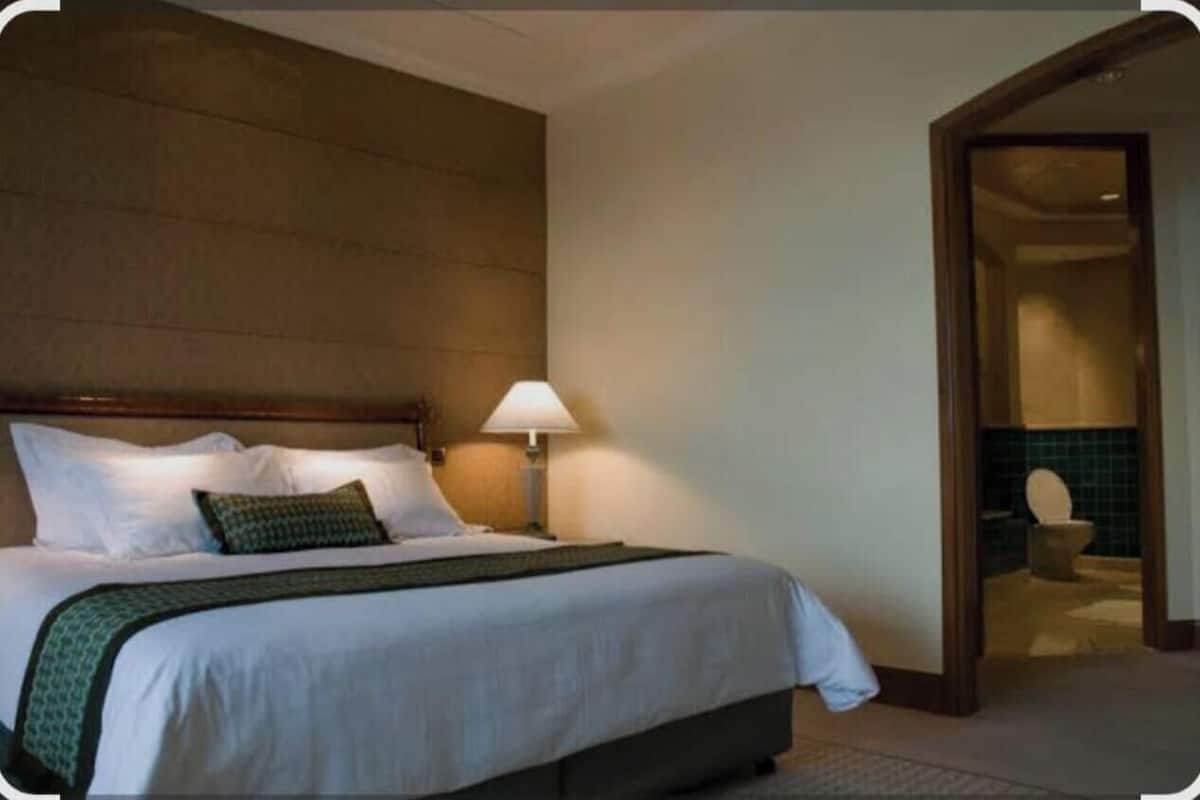 Ein Hotelzimmer mit einem großen Bett, einem Nachttisch, einer Lampe und Blick ins Badezimmer durch eine offene Tür.