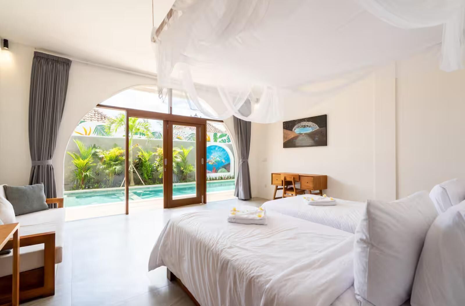 Ein Schlafzimmer mit Bett, Schreibtisch und Blick auf einen Pool und Grünflächen.