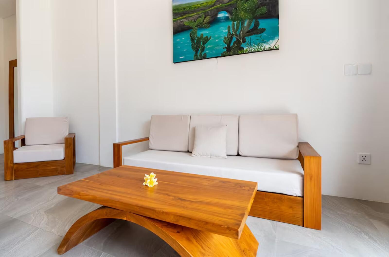 A modern living room with a wooden coffee table, a white sofa with cushions, and a wooden armchair.
