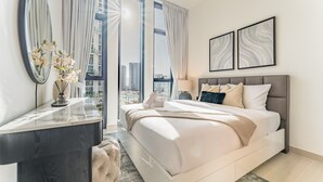 Un dormitorio moderno con una cama grande, un tocador con espejo y vistas a la ciudad a través de amplias ventanas.