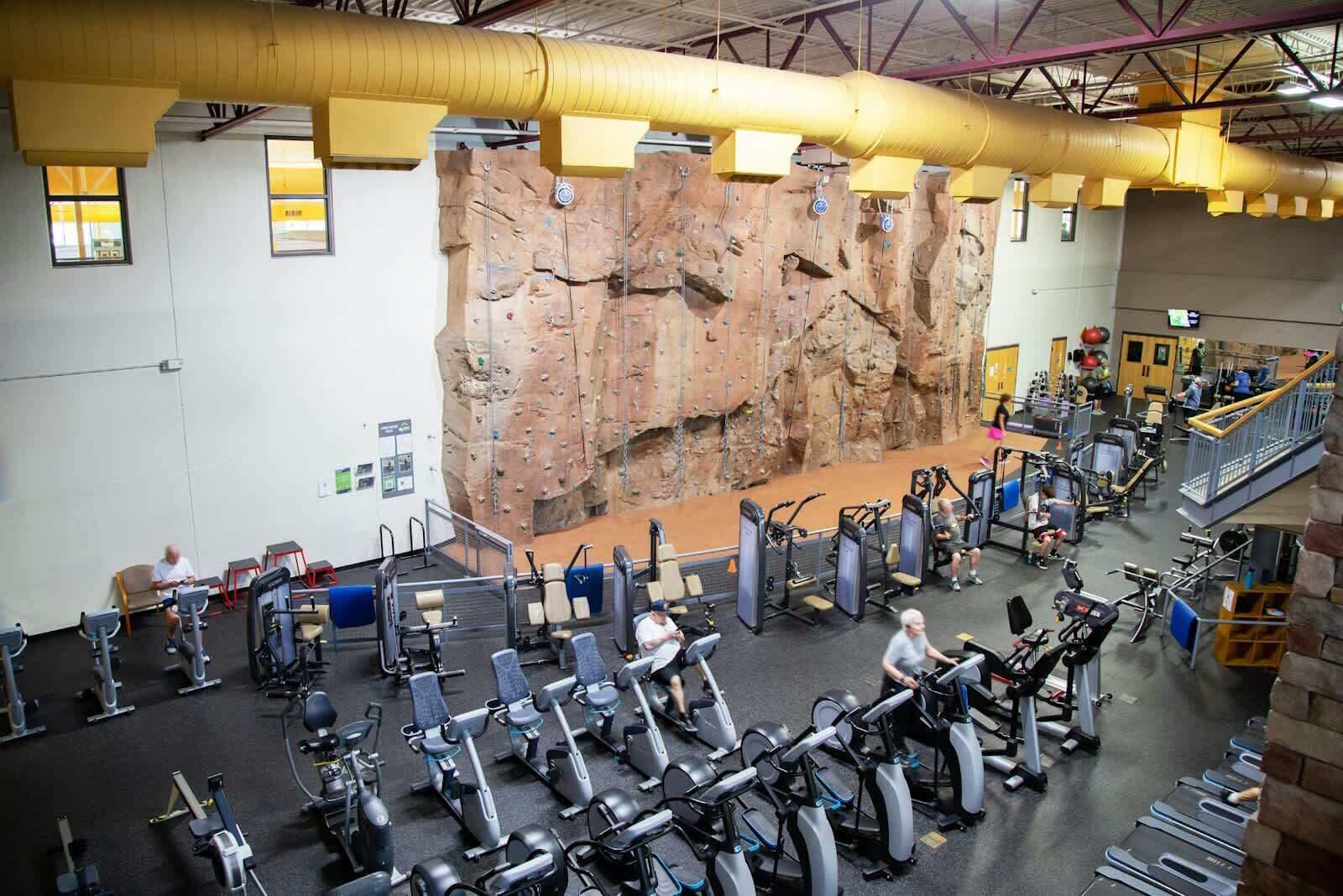 A gym with a climbing wall, exercise equipment, and a staircase.