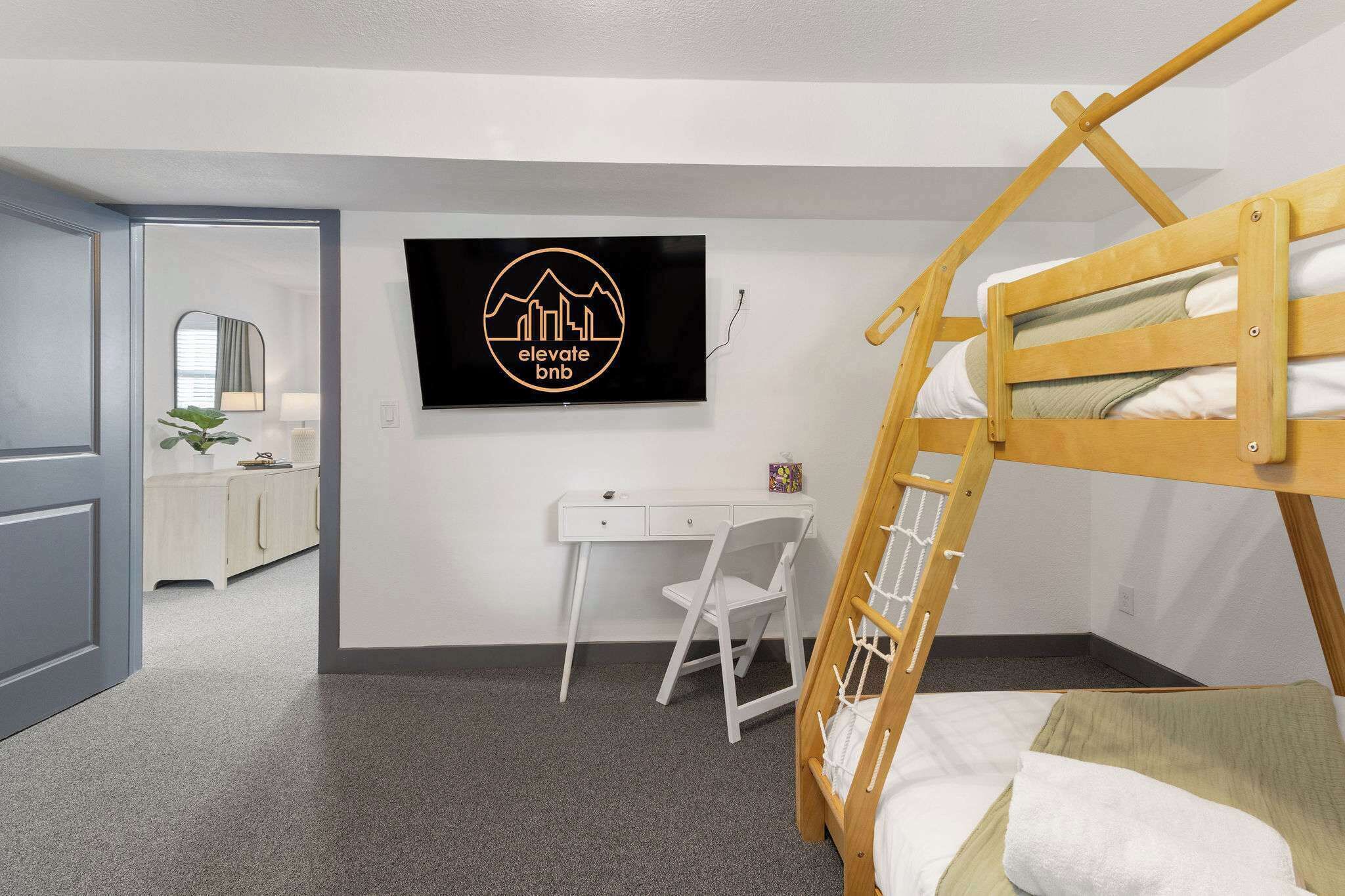 A bedroom with a bunk bed, a desk, and a chair. There is a television mounted on the wall displaying a logo.
