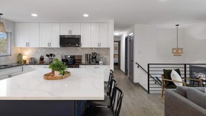 A modern kitchen with white cabinets, a large island, and a dining area with a sofa and chairs.