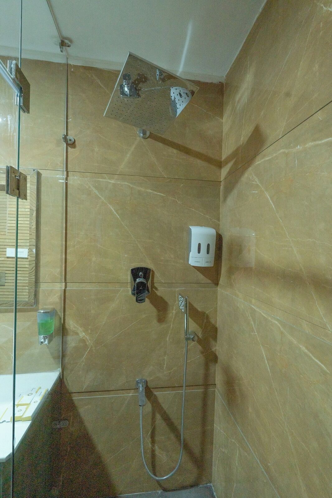A bathroom with a glass shower enclosure, a handheld showerhead, a wall-mounted soap dispenser, and a glass sink.