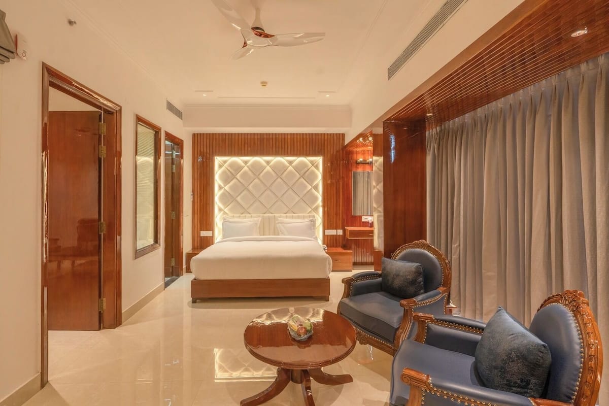 Um quarto de hotel espaçoso, com uma cama grande, um espaço de estar com mesa de centro e vista para a cidade pela janela.