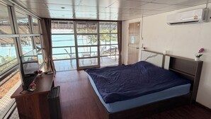 A bedroom with a large bed, a wooden desk, a window with a view of a balcony, and an air conditioning unit on the wall. - Moonlight Bar and restaurant  (Koh Samui)