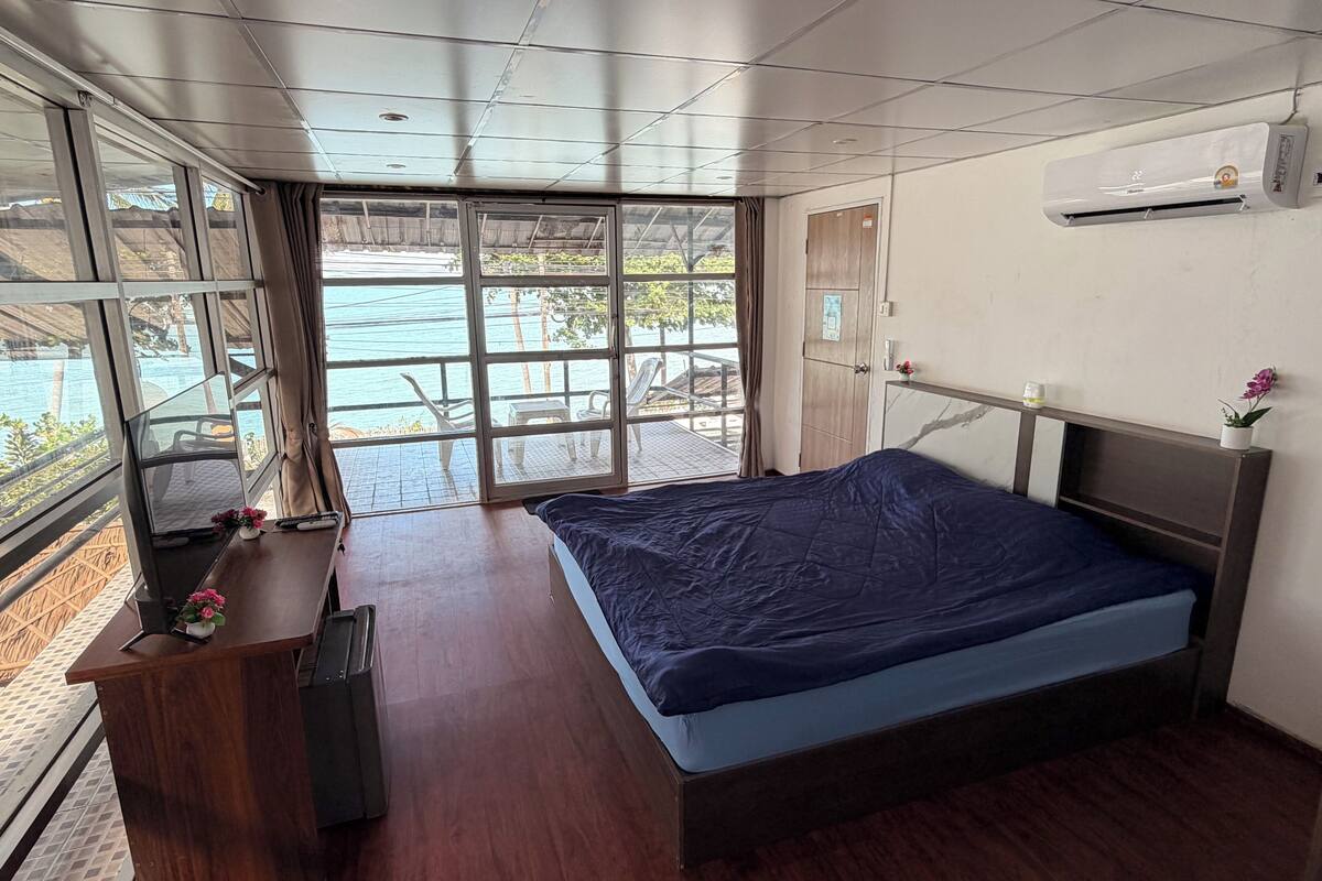 Un dormitorio con una cama grande, un escritorio de madera, una ventana con vistas a un balcón y un equipo de aire acondicionado en la pared.