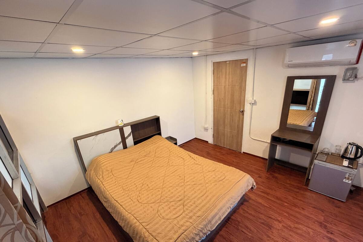 Un dormitorio con cama, escritorio, espejo, armario y equipo de aire acondicionado.