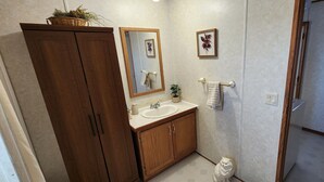 A bathroom with wooden cabinets, a sink, a mirror, and a shower. - Family Getaway in Interior, SD – Just 5 Min to Badlands NP (Interior)
