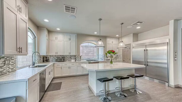 A modern kitchen with white cabinets, a large island with bar stools, stainless steel appliances, and pendant lighting. - Luxury 2 Story 3 Car Garage Home (Las Vegas)