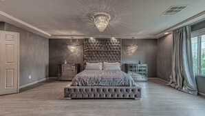 A bedroom with a tufted headboard, a large bed, a nightstand, and a dresser. - Luxury 2 Story 3 Car Garage Home (Las Vegas)