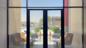 A modern hotel room with a large glass door leading to an outdoor seating area with chairs and tables. - Arjan Park Apartments (Riyadh)