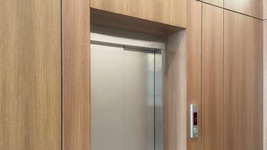 A modern elevator with a metallic interior and a wooden wall panel. - Arjan Park Apartments (Riyadh)