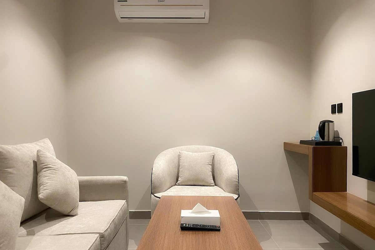 A modern living room with a sofa, a chair, a coffee table, and a flat-screen TV mounted on the wall.