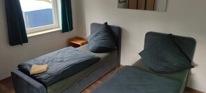 A small, single-bed room with a window, a wooden nightstand, and a wall-mounted mirror.