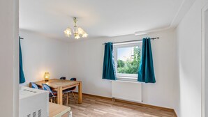 A room with a wooden table, chairs, a ceiling light fixture, a window with curtains, and a radiator. - Apartment 'Yellow A' (Miltenberg)
