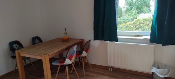 A dining area with a wooden table, colorful chairs, a bottle, and a window with curtains.