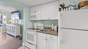 A modern kitchen with white cabinets, a microwave, stove, and refrigerator. - Oceanfront Resort Condo with Balcony (Myrtle Beach)