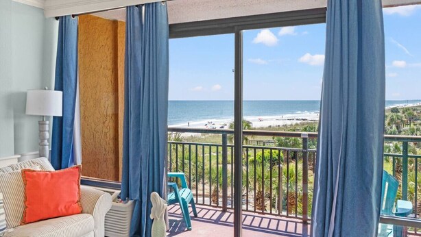 A balcony with a view of the beach, a chair, a table, and a lamp. - Oceanfront Resort Condo with Balcony (Myrtle Beach)