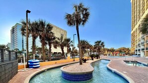 A swimming pool with a circular design, surrounded by palm trees and a brick walkway. - Oceanfront Resort Condo with Balcony (Myrtle Beach)