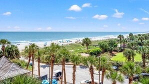 A beach view with palm trees, a pool area, and a clear sky. - Oceanfront Resort Condo with Balcony (Myrtle Beach)