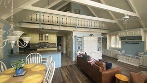 A spacious kitchen with a high ceiling and exposed beams, a dining area with a wooden table and chairs, and a cozy seating area with a sofa and armchairs.