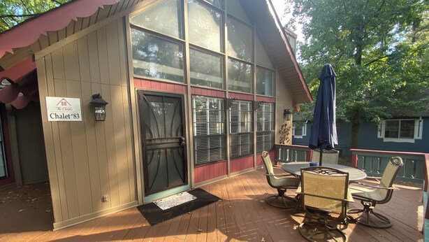 A building labeled "Chalet #83" with large windows, a covered patio with outdoor furniture, and a sign indicating it is part of "The Chalet's" property.