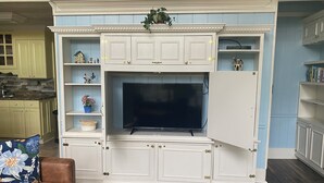 A living room with a built-in TV, white cabinetry, and a floral-patterned couch.