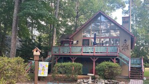 A two-story wooden cabin with a balcony, surrounded by trees.