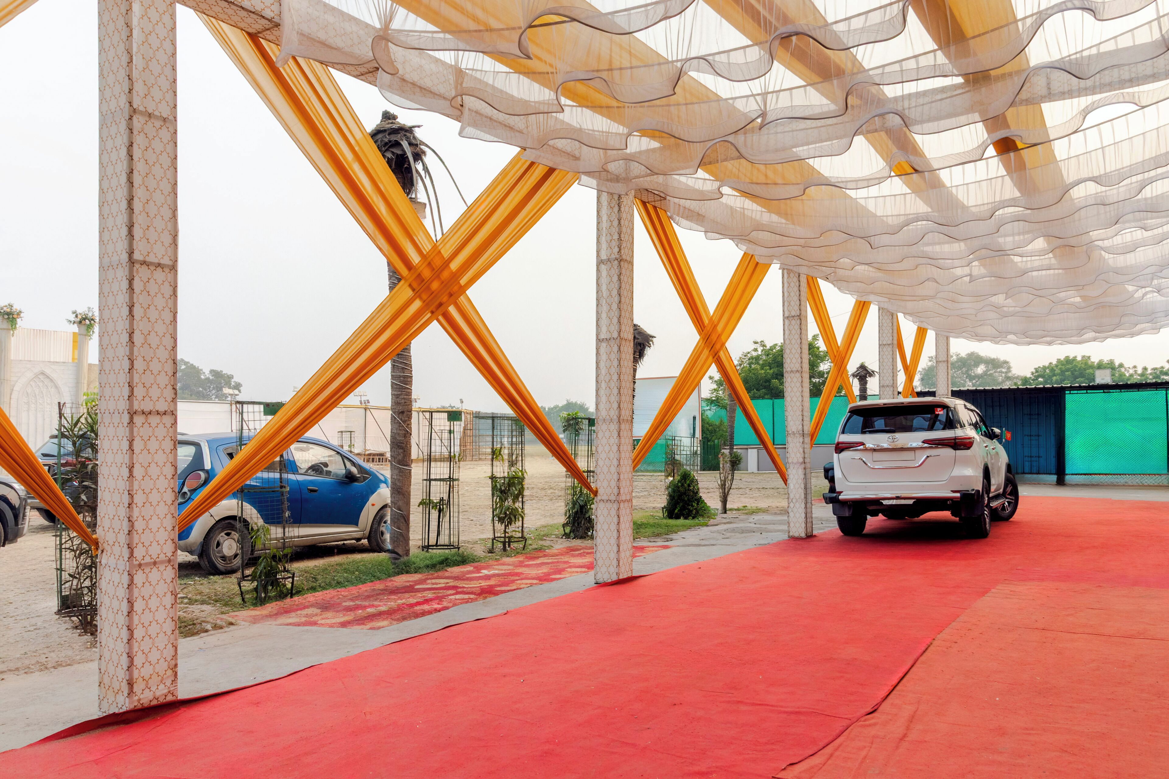 A covered outdoor area with a red carpet, two cars parked, and a green building in the background.