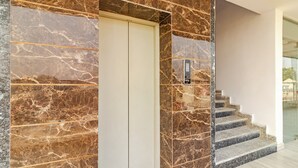 A marble-floored staircase leading to a white elevator door with a control panel. - Treebo KGF Villa with Swimming Pool (Prayagraj)