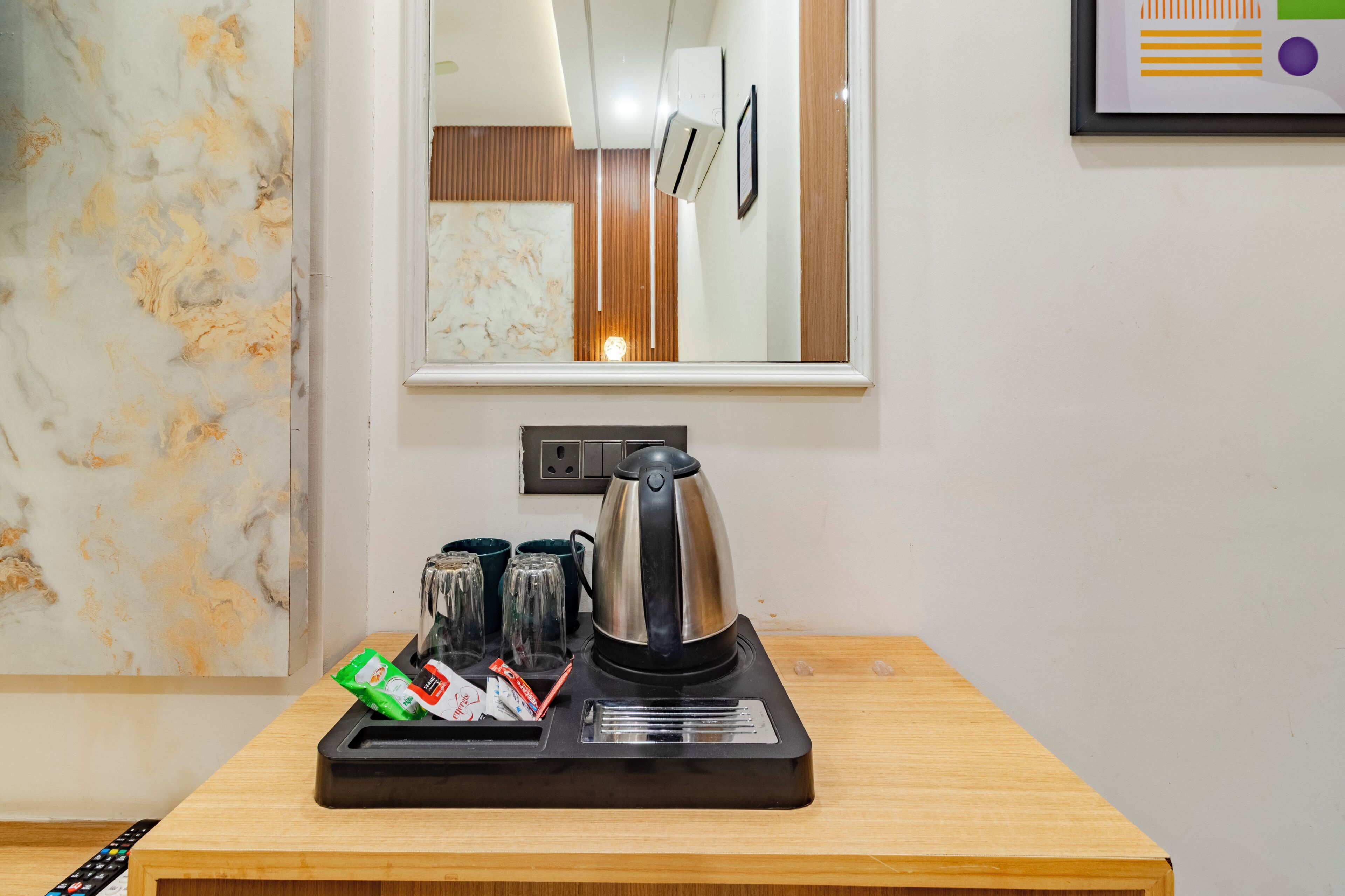 Habitación de hotel con pared de mármol, cafetera, bandeja con tazas y condimentos, y un cuadro enmarcado en la pared.