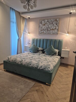 A bedroom with a bed, a nightstand, a wall-mounted light, a ceiling fan, and a window with curtains.