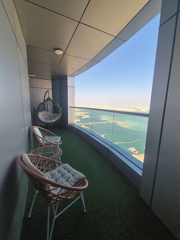 A balcony with wicker chairs, a hanging chair, and a view of a coastal landscape.
