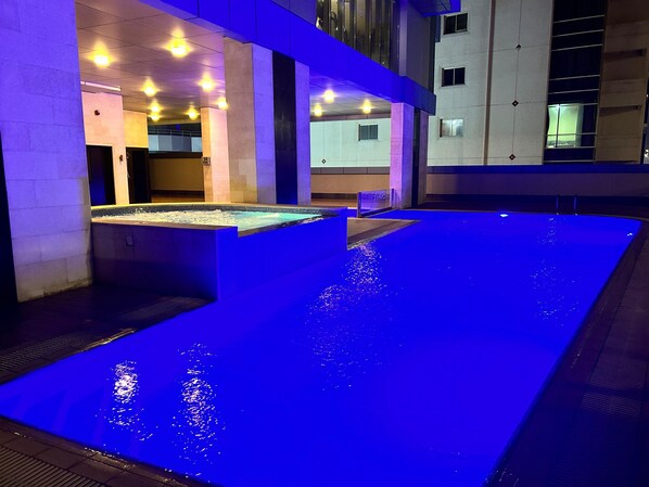 A swimming pool with a blue-lit edge, surrounded by a building with multiple floors and a tiled floor. - Era View - Sea and City View - Private Balcony (Manama)