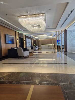 A modern hotel lobby with a reception desk, seating area, and a large chandelier.