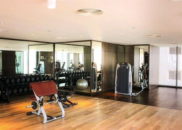 Un gimnasio moderno con paredes espejadas, equipamiento de ejercicio y suelo de madera.