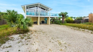 A two-story house with a balcony, surrounded by gravel and greenery.