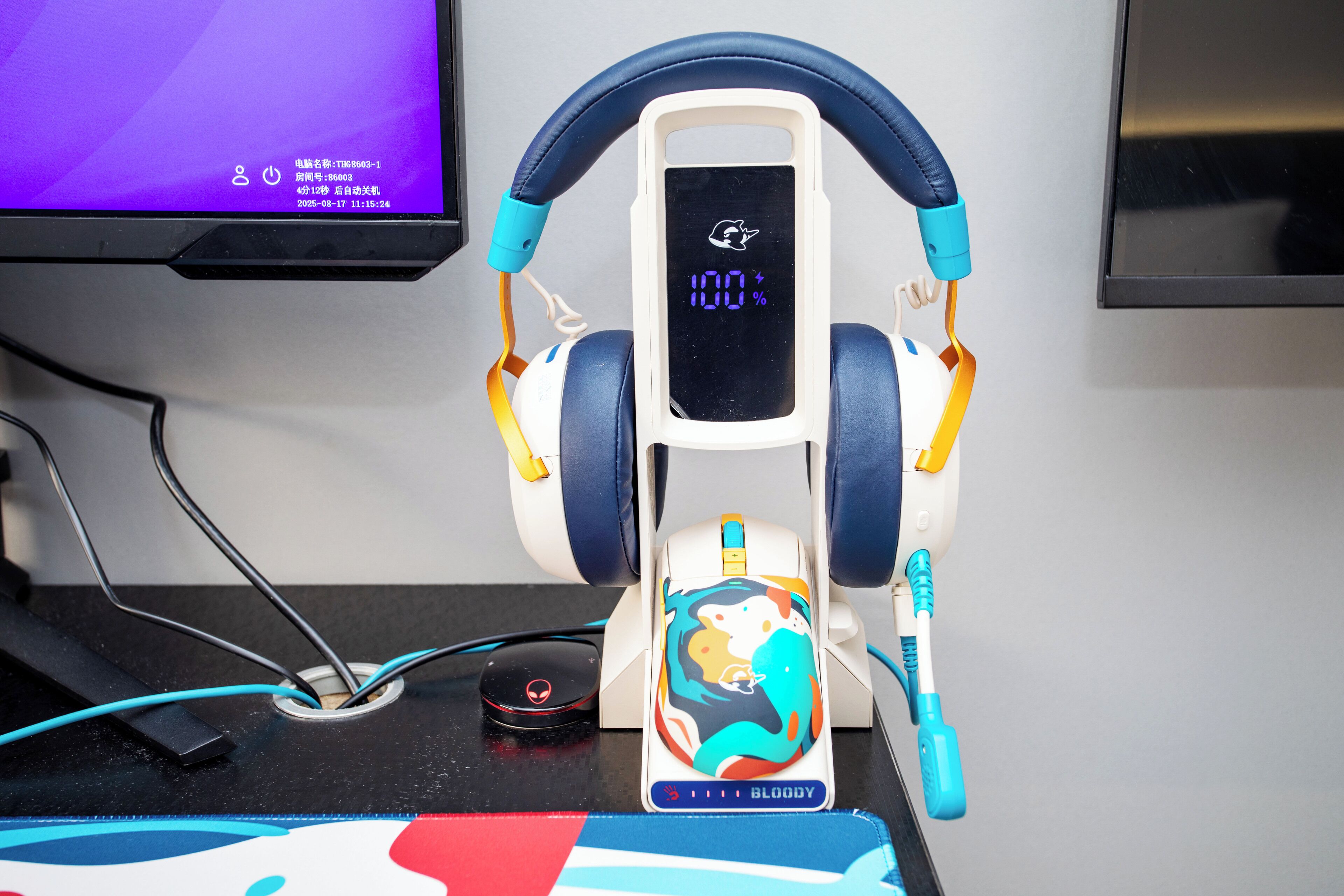 A pair of headphones on a stand with a colorful design, a charging cable, and a digital display.