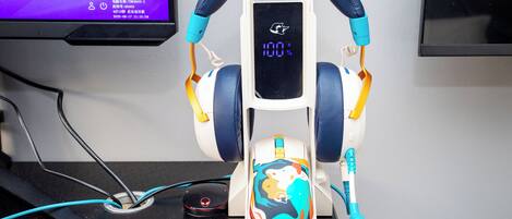 A pair of headphones on a stand with a colorful design, a charging cable, and a digital display.
