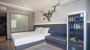 A modern hotel room with a large bed, a seating area, and a minibar.