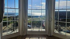 Een kamer met grote ramen en uitzicht op een kustgebied, inclusief een pier en een toren.